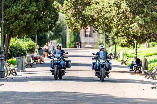 Rome, Italy - September 4, 2018: Historic green city park on Via della Domus Aurea street with security police officers on motorcycles emergency driving on road by Colosseum, sunny summer day
