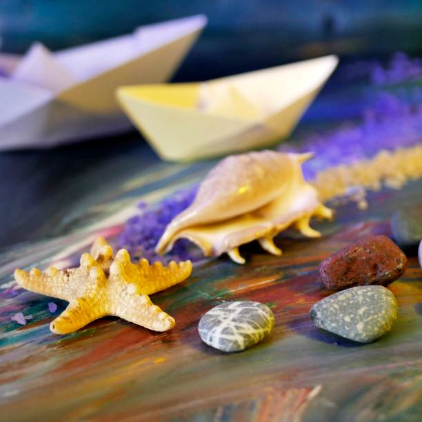 Decorative composition installation - smooth sea stones, sea salt, shells, starfish and paper boats on a blue background