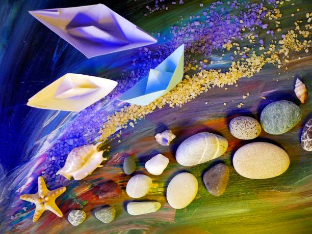 istock Decorative composition installation - smooth sea stones, sea salt, shells, starfish and paper boats on a blue background 1059717442