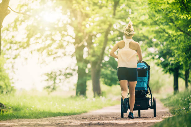 Running woman with baby stroller enjoying summer in park stock photo