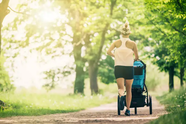 Photo of Running woman with baby stroller enjoying summer in park