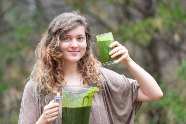 istock Young woman outside, outdoors, holding plastic blender container for smoothie with green vegetables, ready to drink with drinking glass in one hand 1059722510