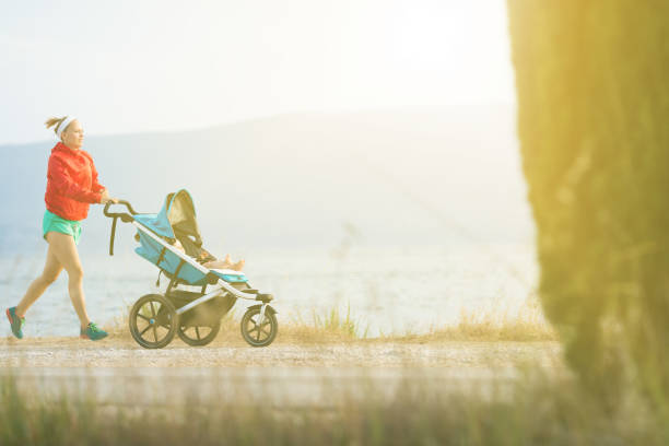Running super mother with child in baby stroller enjoying sunset and mountains landscape. Jogging or power walking supermom, active family at sunset. Beautiful inspirational mountains landscape.