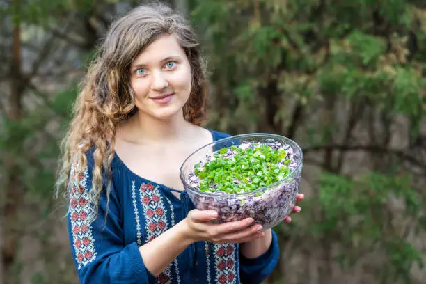 Young woman outside, outdoors, holding glass bowl full of homemade red, purple cabbage salad with green onions, scallions