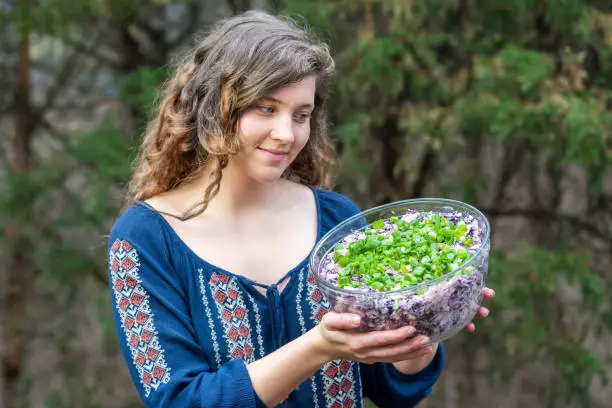 Young woman outside, outdoors, holding glass bowl of homemade red, purple cabbage salad dish with green onions, scallions