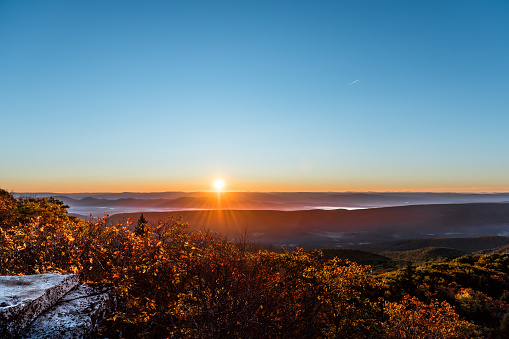Bear rocks overlook sunrise, sunburst, sunrays, rays, sun above mountains in autumn with rocky landscape in Dolly Sods, West Virginia with orange, yellow foliage trees, mountains, hills