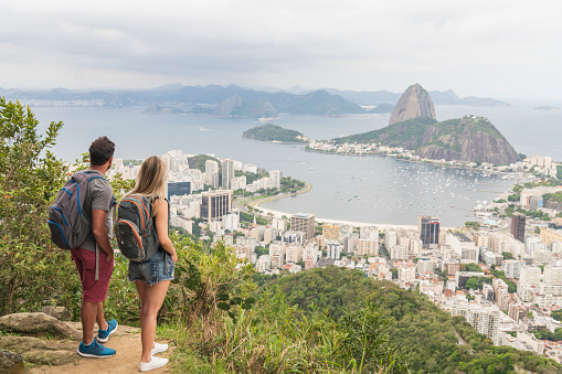 Backpacking tourists standing with views of Sugar Loaf Mountain in Rio de Janeiro, boyfriend and girlfriend backpackers with rucksacks, looking at view