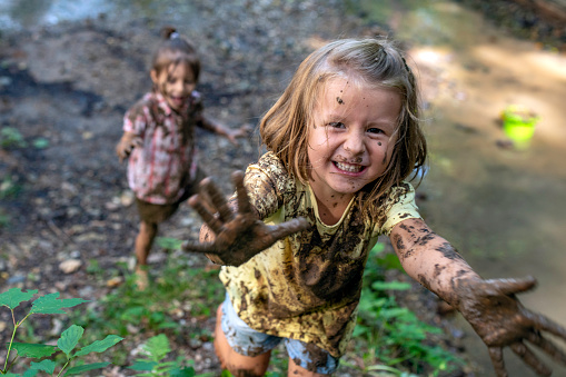 Smiling little muddy girl looking at camera and showing palms to a photographer.