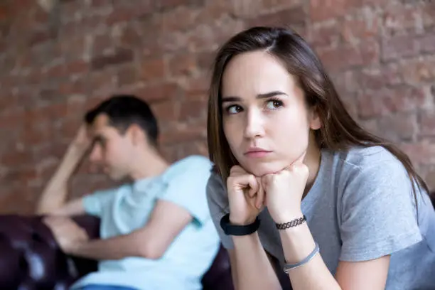 Photo of Offended man and woman are seated separately on sofa.