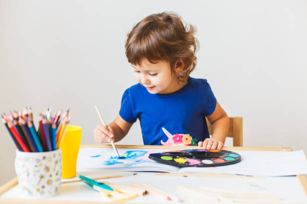 niña de 3 años pintando en la pequeña mesa en la casa. - 4 5 years fotografías e imágenes de stock