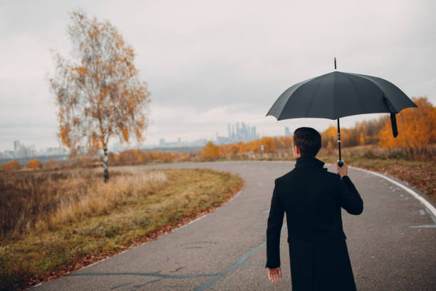 istock Young man in black coat walking in the rain with umbrella 1059741902