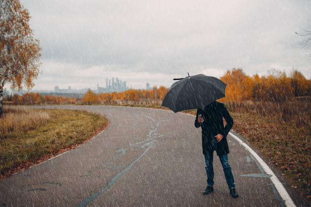 istock Young man in black coat walking in the rain with umbrella 1059741932