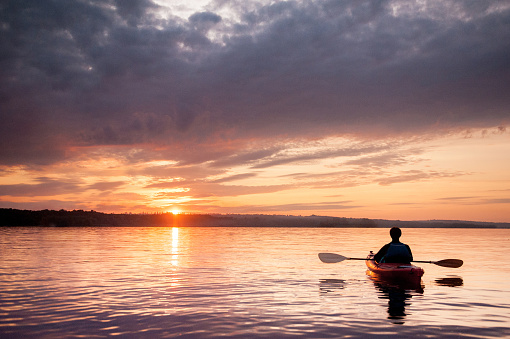 Man in a kayak on the river on the scenic sunset