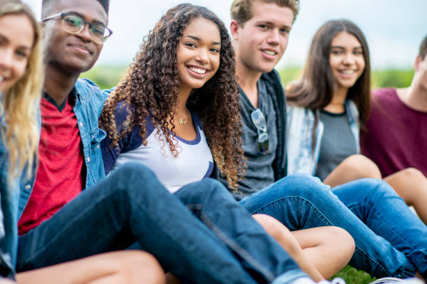 Friends pose for a photo A diverse group of friends sits on the grass with their hands wrapped around each other. They are looking at the camera and smiling. teenagers only photos stock pictures, royalty-free photos & images