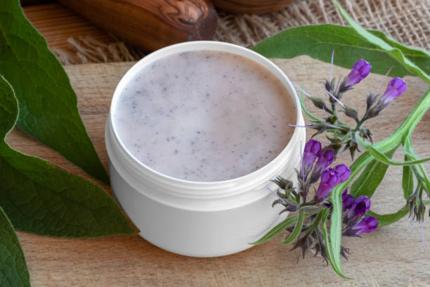 A jar of homemade comfrey root ointment with fresh comfrey plant