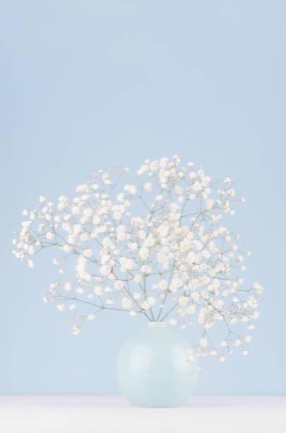 istock Spring branch with small white flowers in blue sphere vase in soft light blue modern interior, on a white table, vertical. 1059757550
