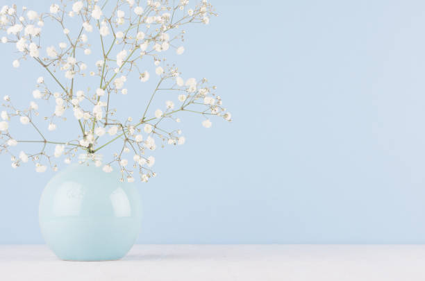 istock Spring branch with small white flowers in blue sphere vase in soft light blue modern interior, on a white table. 1059757674