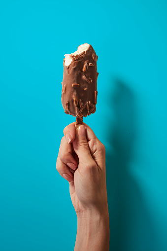 Hand holding Chocolate Almonds Ice Cream Bar isolated on Blue Background