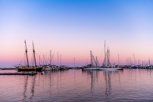 As the sun falls, a pink inversion layer forms behind a bay of sailboats, framing a maritime classic image.