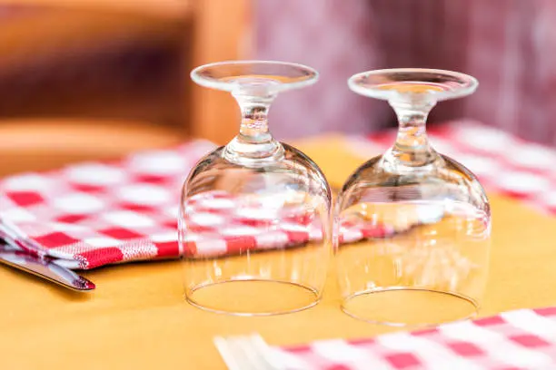 Macro closeup of two glasses glass upside down on restaurant table in Rome, Italy, Italian outside in traditional style street cafe red and white checkered tablecloth