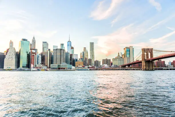 Outdooors view on NYC New York City Brooklyn Bridge Park by east river, cityscape skyline at sunset, skyscrapers, buildings, waves, reflection, orange clouds