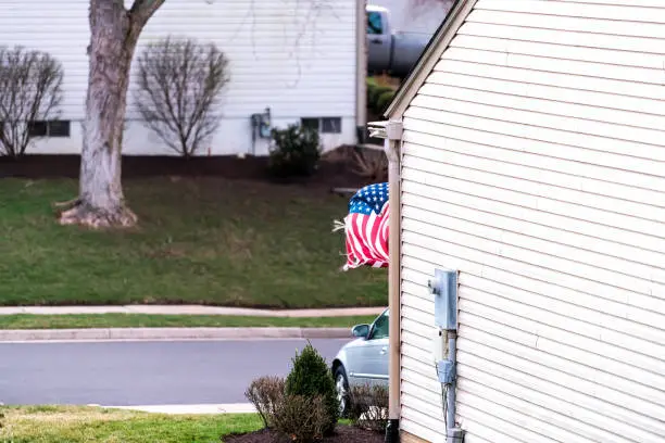 Residential neighborhood in United States, Virginia with house, home, car garage parking, street, road, waving in wind American flag, rag, ragged, weathered, old, broken