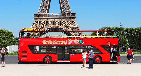 Paris, France - June, 2018: Red double decker bus with tourists in Paris near the Eiffel Tower. Citysightseeing logo, city tour. Blue sky, panoramic view