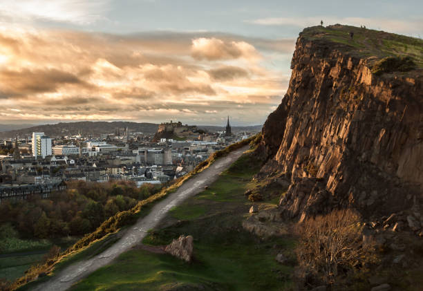 Landscape view of the Salisbury Crags and Edinburgh's Castle from Holyrood Park at sunset. Cityscape. Travel View of the Salisbury Crags at Holyrood Park, in Edinburgh, Scotland, with Edinburgh's Castle in the background, and evening light on the face of the cliffs and the clouds. Landscape. Cityscape. Travel. arthurian legend stock pictures, royalty-free photos & images