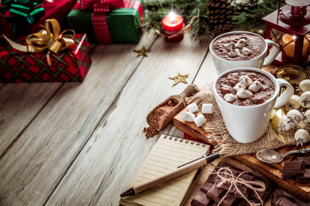 istock Homemade hot chocolate mugs with marshmallows on rustic wooden table with candlelight and note pad. Christmas themes. 1059798730