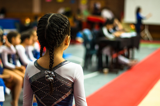 Little gymnast waving to the public in a competition at the stadium