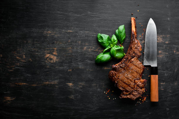 istock Steak on the bone. tomahawk steak On a black wooden background. Top view. Free copy space. 1059836316