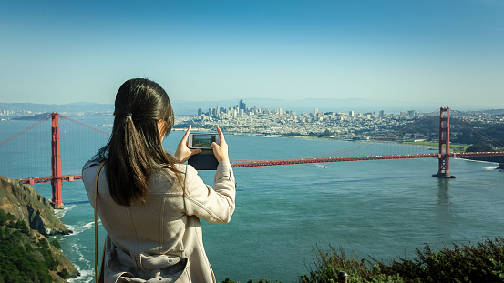 Girl taking a photo of San Francisco and Golden Gate bridge with an iphone