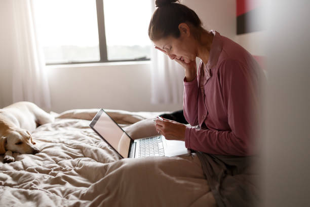 Sick woman on bed video chatting with doctor on laptop Sick woman making an appointment with doctor via internet with her dog on bed insurance pets dog doctor stock pictures, royalty-free photos & images