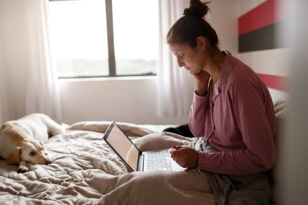 Sick woman on bed video chatting with doctor on laptop Sick woman making an appointment with doctor via internet with her dog on bed insurance pets dog doctor stock pictures, royalty-free photos & images