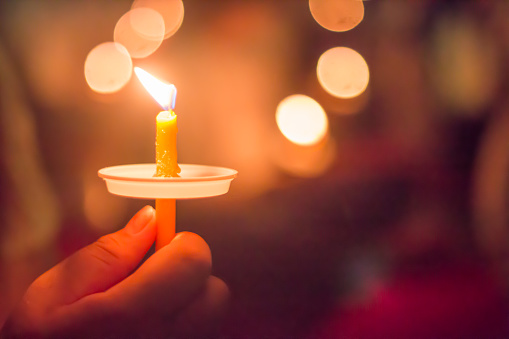 hand holding a burning candle with bokeh background