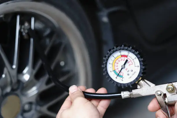 Photo of Close up mechanic inflating tire hand holding gauge pressure for checking and filling air in car tire. Automobile concept.