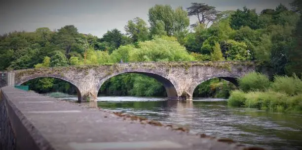 A beautiful stream passing through the arch bridge in ireland, with green nature around it.