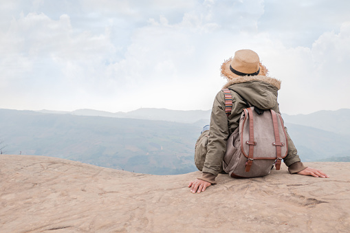 Hipster girl with backpack sitting in a rocky top of the mountain against the blue of sky