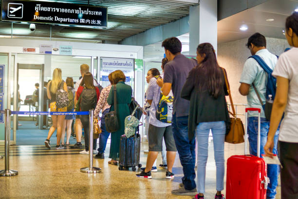 People waiting in line for security check at airport domestic departures Krabi, Thailand - September 28, 2018:  Many people are waiting in line at Krabi airport departure area, Thailand.  Holding luggage and suitcases.  They await a security screening prior to boarding a flight.  These security systems were introduced to combat terrorism by the Transport Security Administration. metal detector security stock pictures, royalty-free photos & images