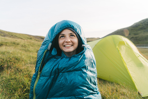 Young Caucasian woman sitting in sleeping bag near the tent in Iceland