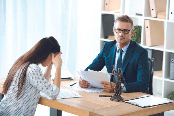 istock lawyer holding papers and looking at camera while sad female client sitting in office 1059944126