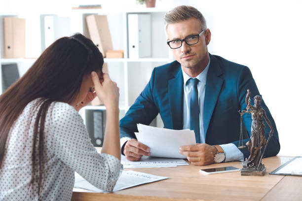 istock lawyer holding papers and looking at camera while working with sad female client 1059944138