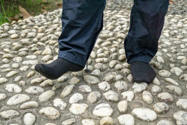 walking on pebble stones Man wearing black socks, walking on pebble stones on the pavement for foot reflexology reflexology stone massaging human foot stock pictures, royalty-free photos & images