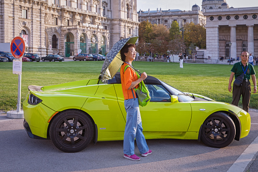 Maria Theresien Platz, Vienna, Austria - September 19, 2018: Female tourist having her picture taken with a fancy car, a Tesla