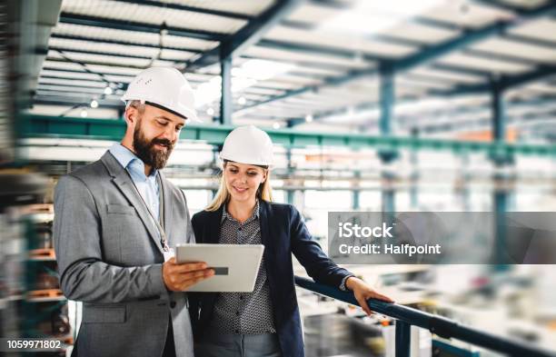 Un Retrato Del Ingeniero Industrial Del Hombre Y La Mujer Con La Tablet En Una Fábrica Trabajando Foto de stock y más banco de imágenes de Industria