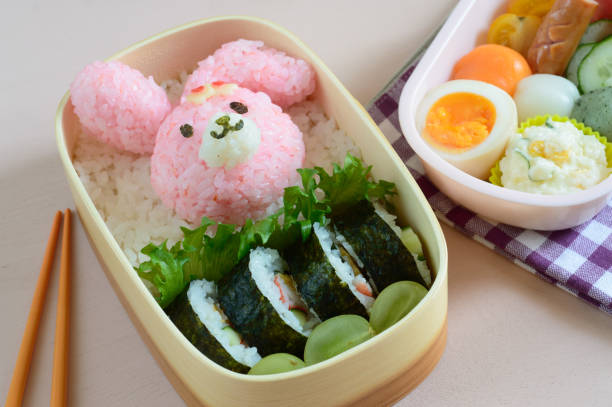 a cute and delicious looking lunch box (bento) consisting of rice ball, sushi roll, boiled egg and the assortment of vegetable