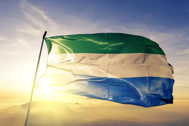 Photo of Sierra Leone Leonean flag textile cloth fabric waving on the top sunrise mist fog