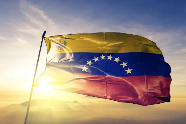 Venezuela Venezuelan Bolivarian Republic flag on flagpole textile cloth fabric waving on the top sunrise mist fog