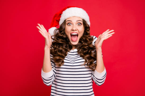 hulst van de merry x mas portret van gekke koele vrolijk blij positieve optimistisch charmante curly-haired meisje in casual gestreepte pullover klappen palmen wachten geschenk geïsoleerd op rode achtergrond - christmas people stockfoto's en -beelden