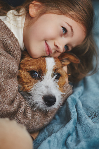 Cute Little smiling Girl with blue eyes hugging a puppy at home.